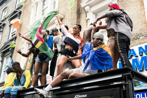 Um grupo de pessoas reunido em cima de um abrigo com bandeiras no Notting Hill Carnival
