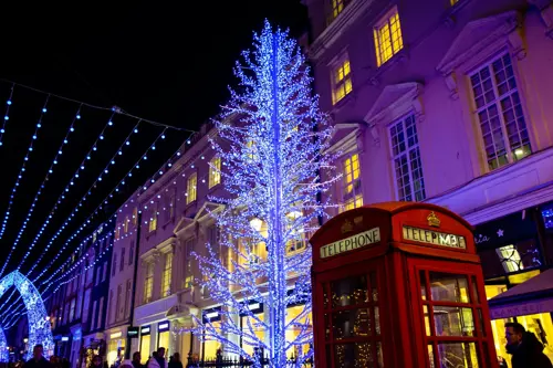 Uma cabine telefónica vermelha de Londres em primeiro plano com uma árvore de Natal branca numa rua de Londres